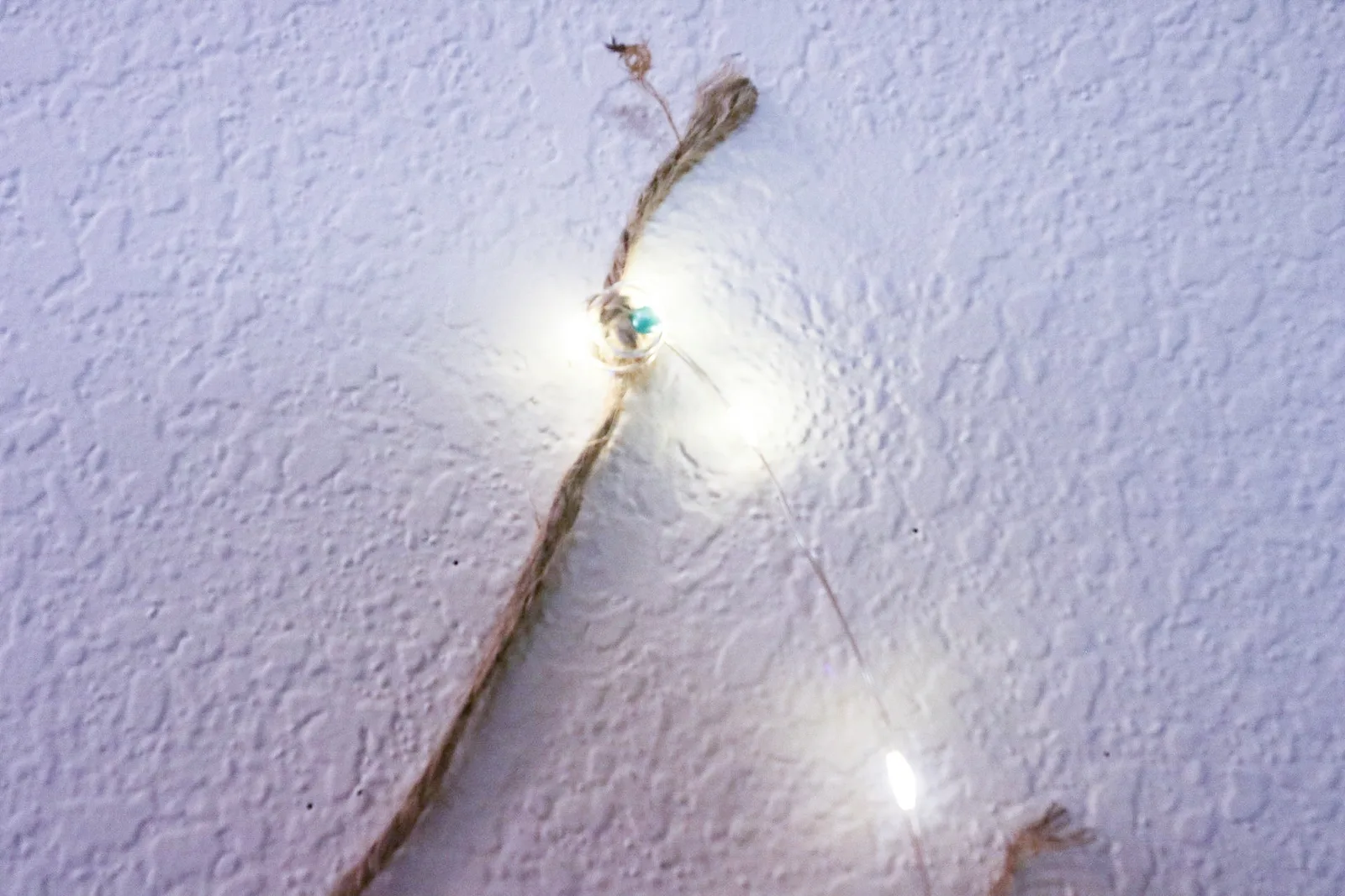 A length of jute twine on a white wall with warm fairy lights wound along it, held up without nails